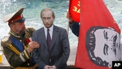 Туристер көп жүретін жерде екінші Николай патша болып киінген (сол жақта) адам картоннан жасалған Владимир Путиннің бейнесін орнатып жатыр, оған Иосиф Сталиннің суреті салынған қызыл ту ұстаған адам көмектесіп тұр. Мәскеу, 13 шілде, 2012 жыл.