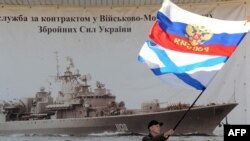 Un bărbat flutură un drapel rusesc și steagul marinei ruse în fața cartierului general al marinei ucrainene de la Sevastopol, 3 martie 2014.